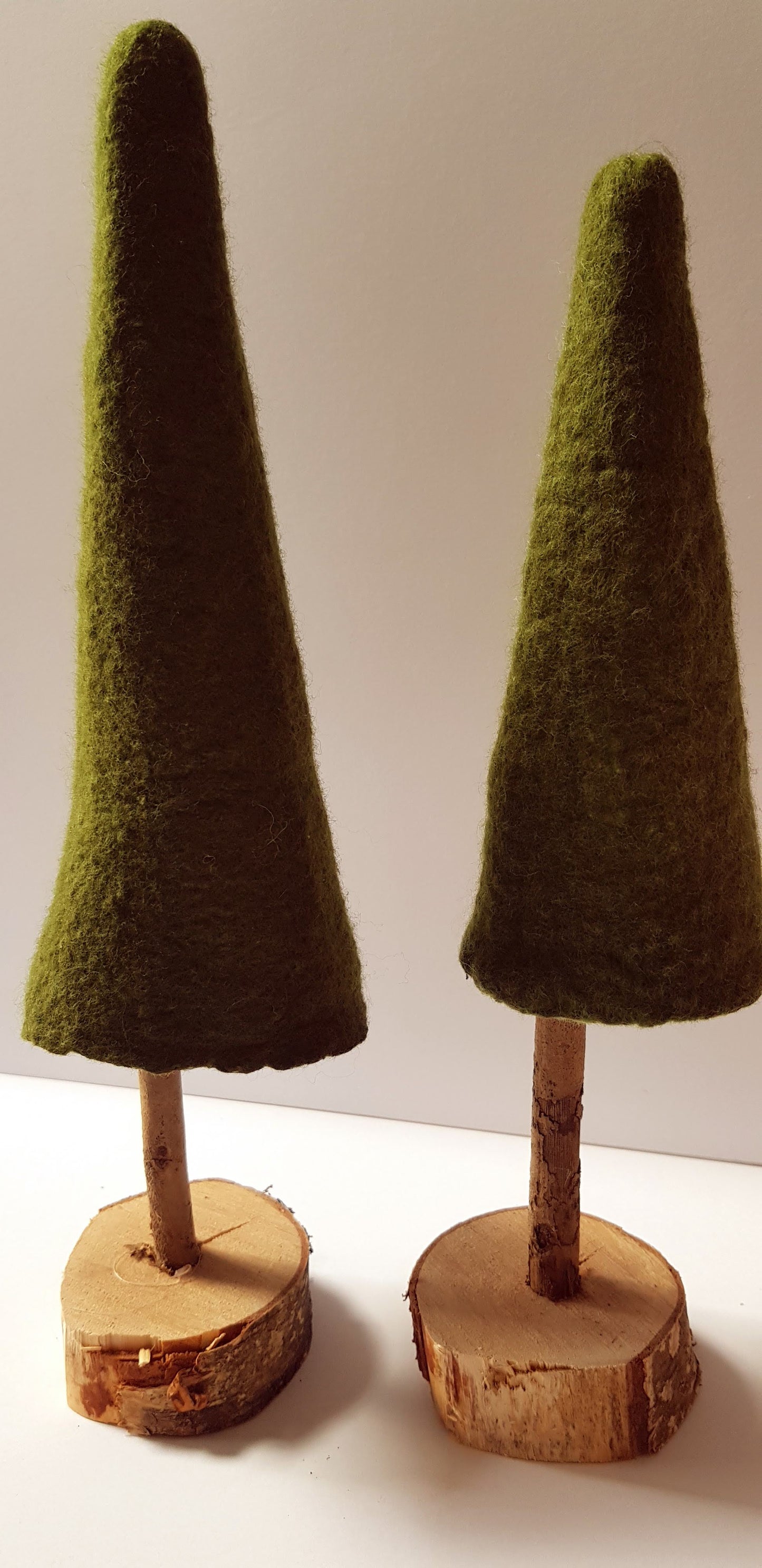 Two decorative cones with green felt tops and wooden bases on a white background