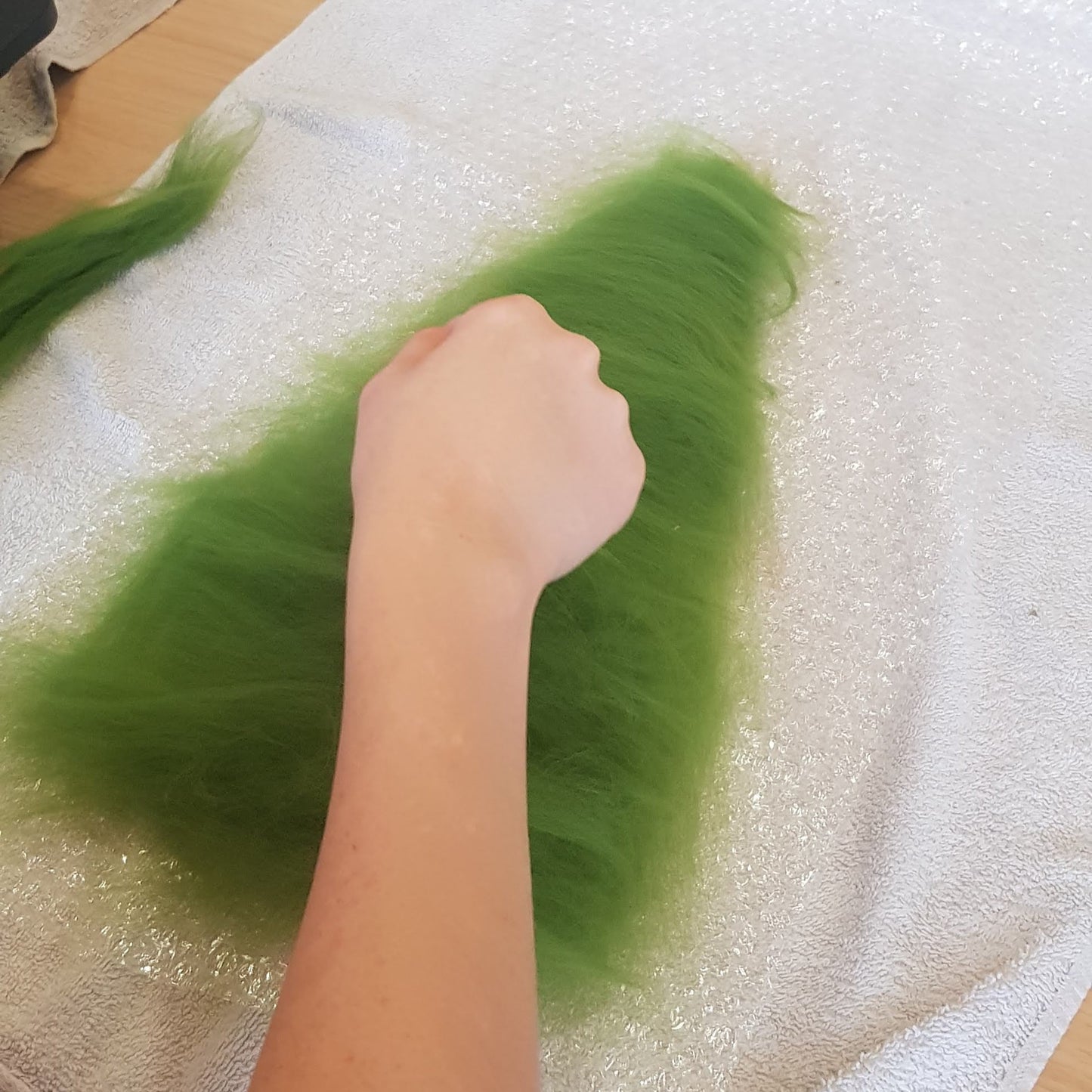 Person handling green material on a table with bubble wrap