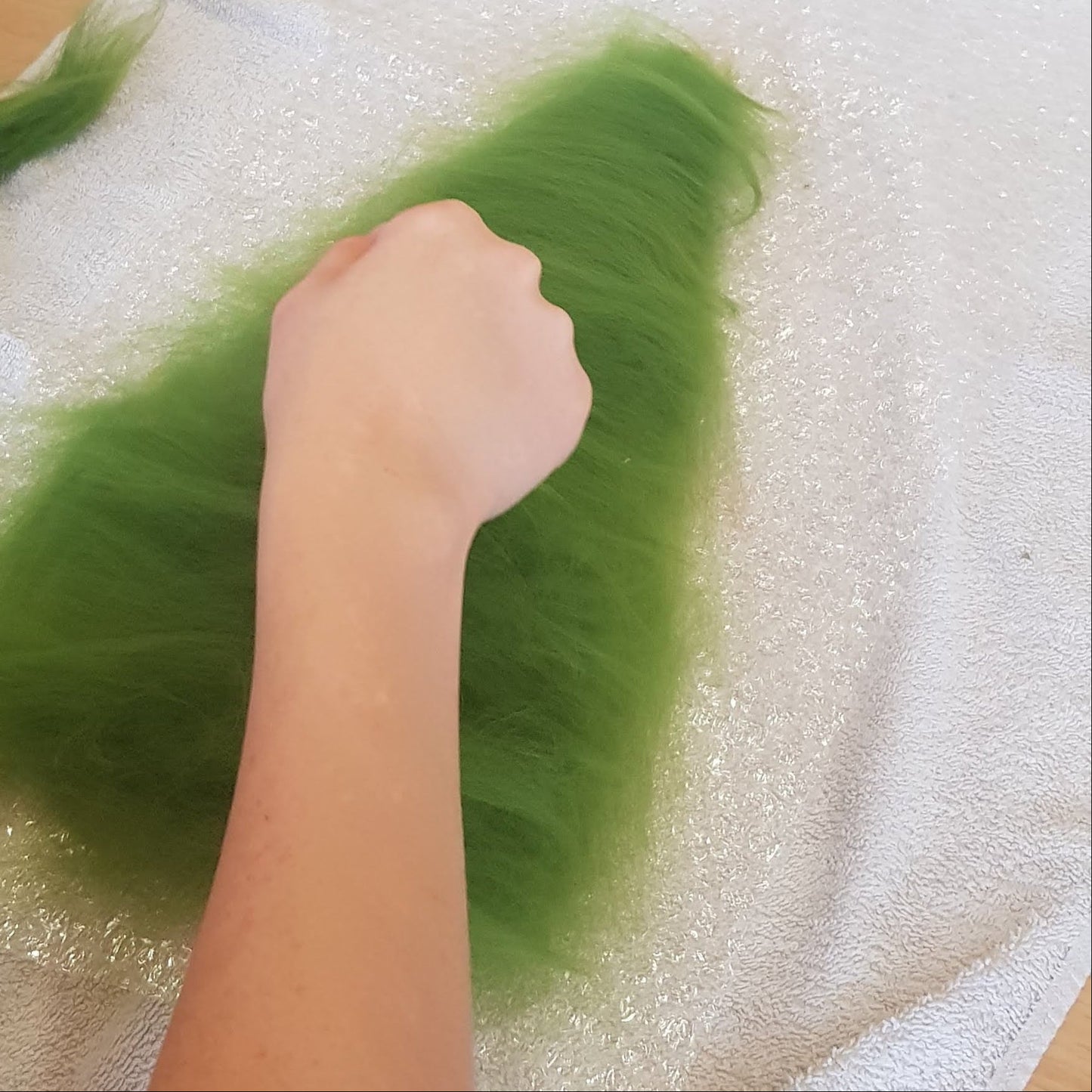 Person handling green material on a table with bubble wrap