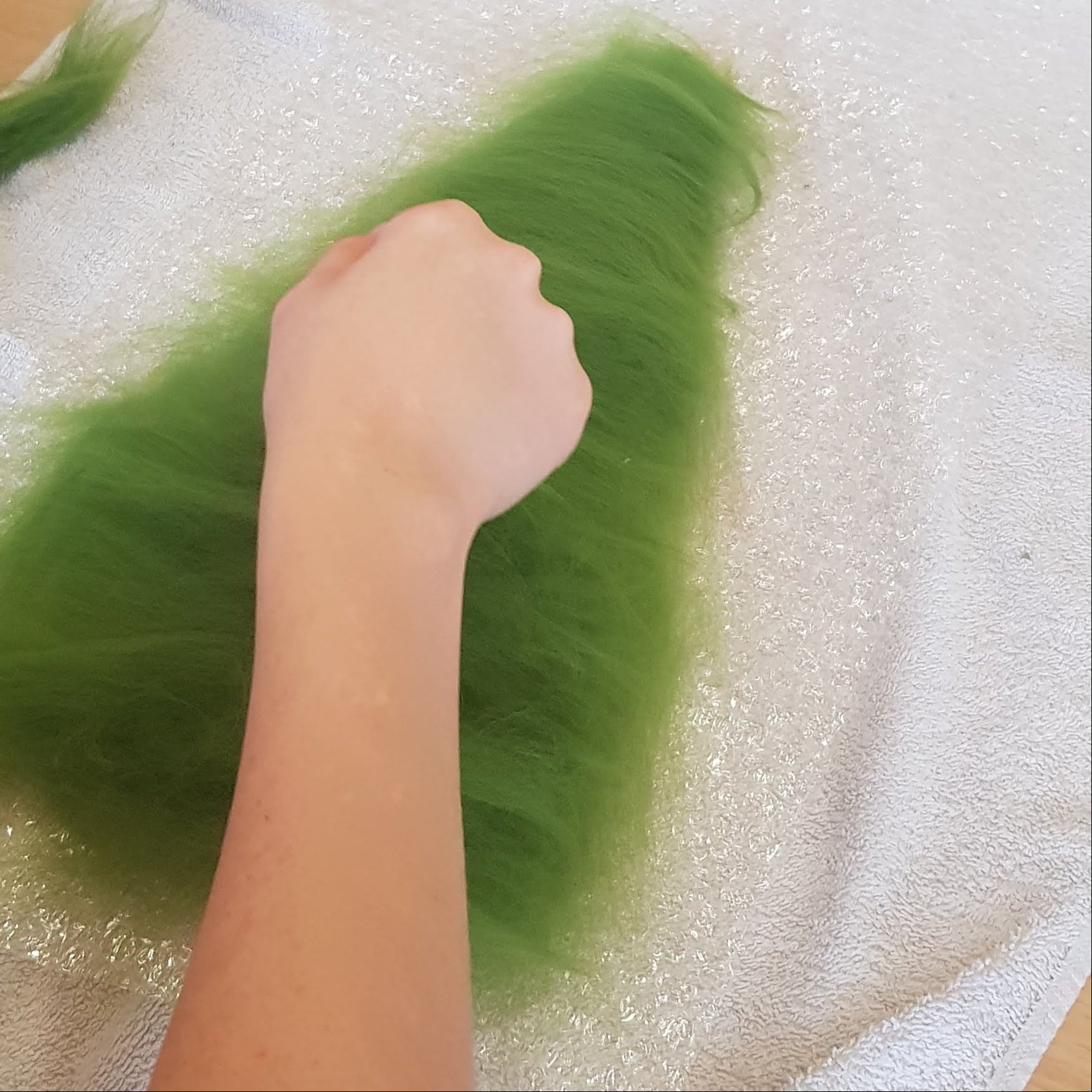 Person handling green material on a table with bubble wrap