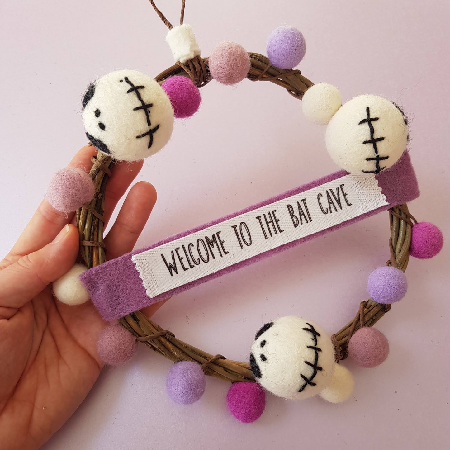 Decorative wreath with zombie face ornaments and 'Welcome to the Bat Cave' banner on a pink background