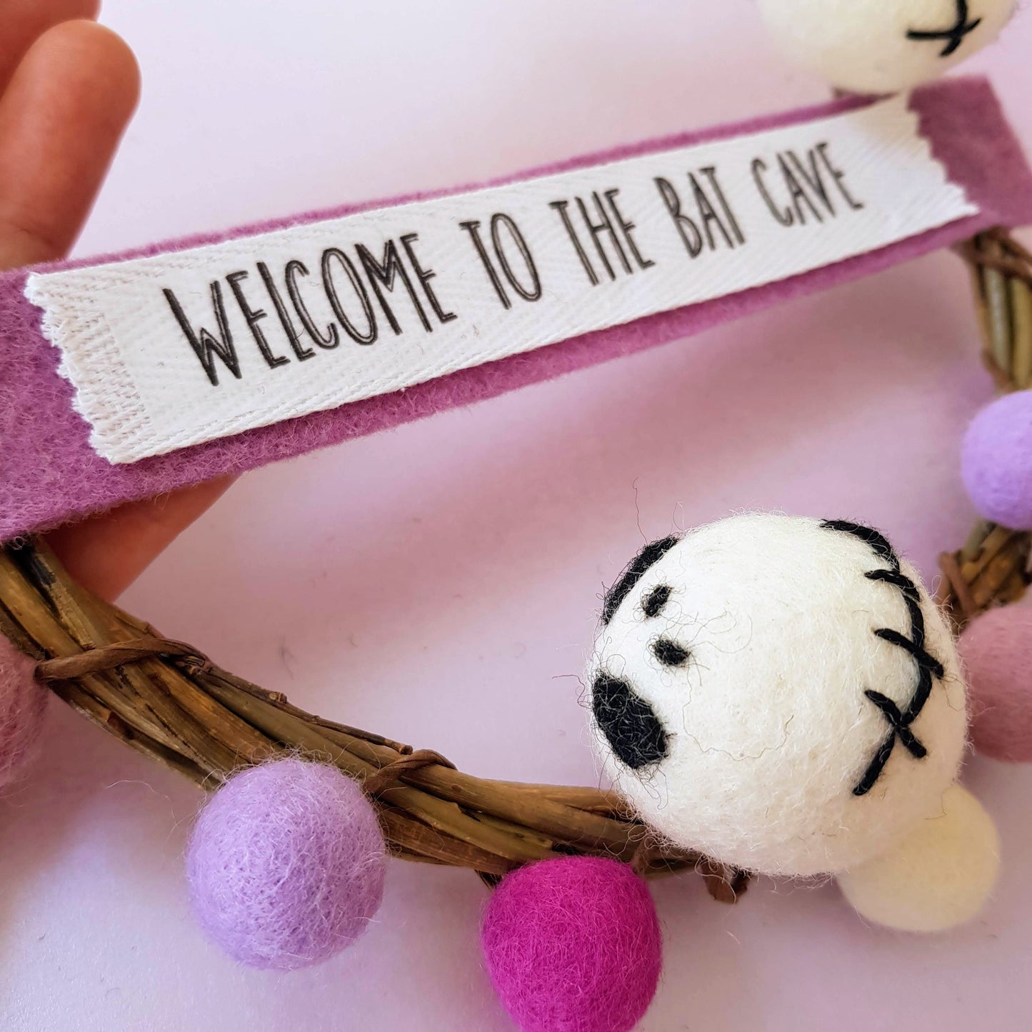 Decorative wreath with a plush toy and 'Welcome to the Bat Cave' sign on a pink background