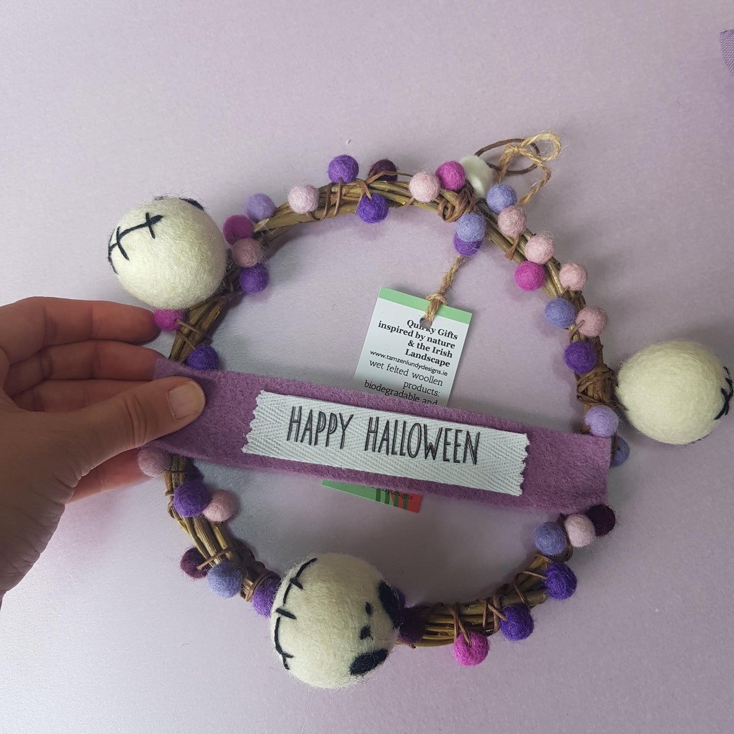 Halloween-themed keychain with pom-pom details and a visible brand tag on a light purple background.