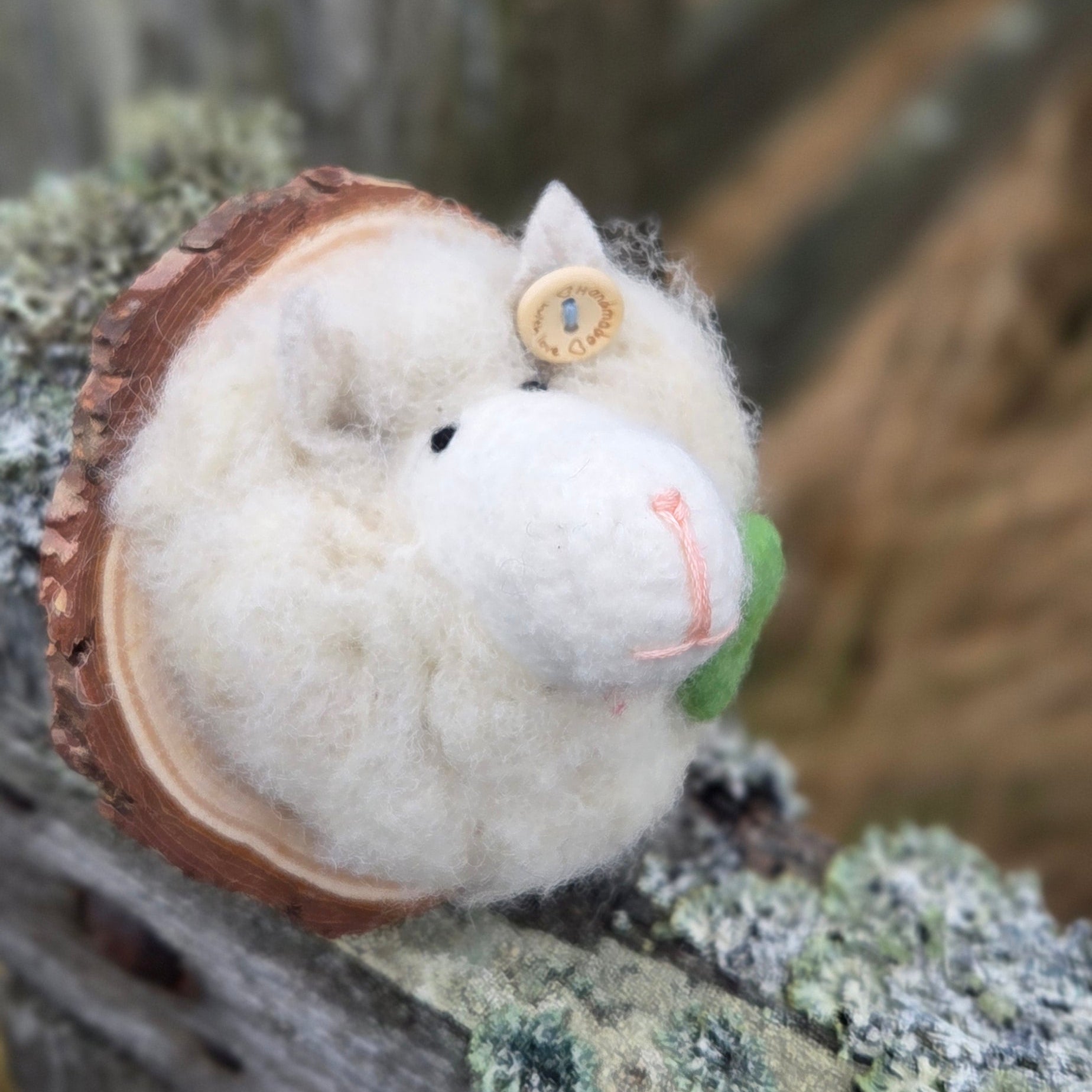 Small white decorative sheep with a green tag on a wooden surface with lichen.