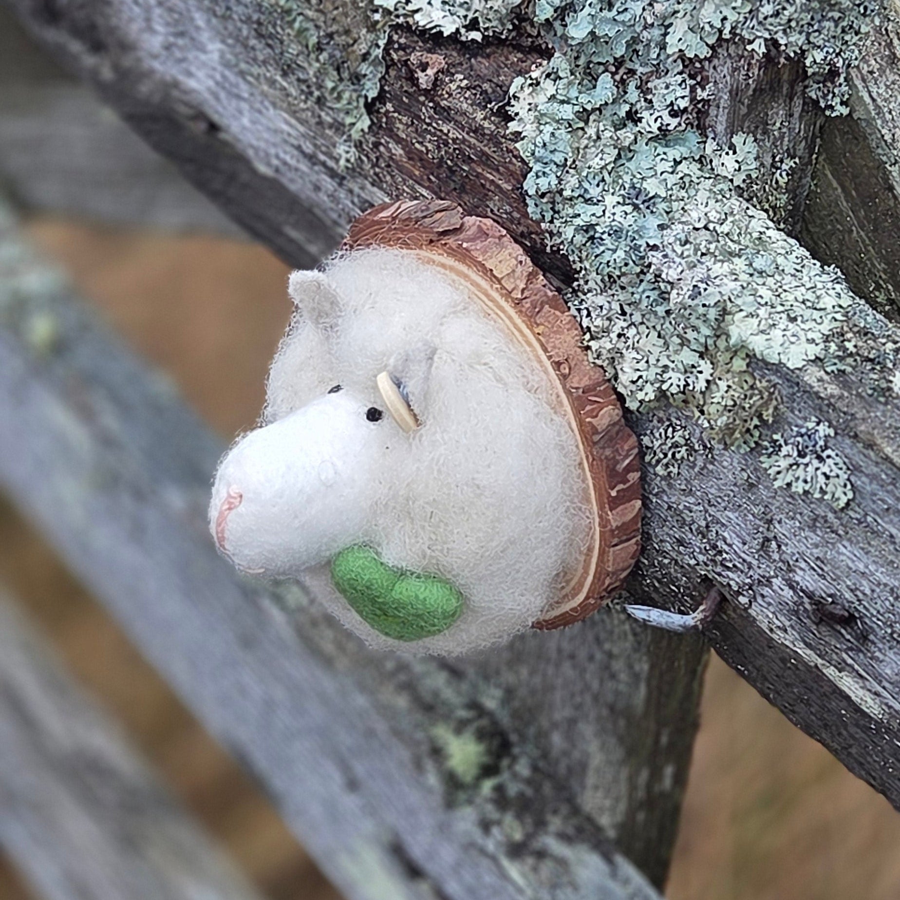 Small white sheep figurine with a green nose on a wooden branch with lichen.