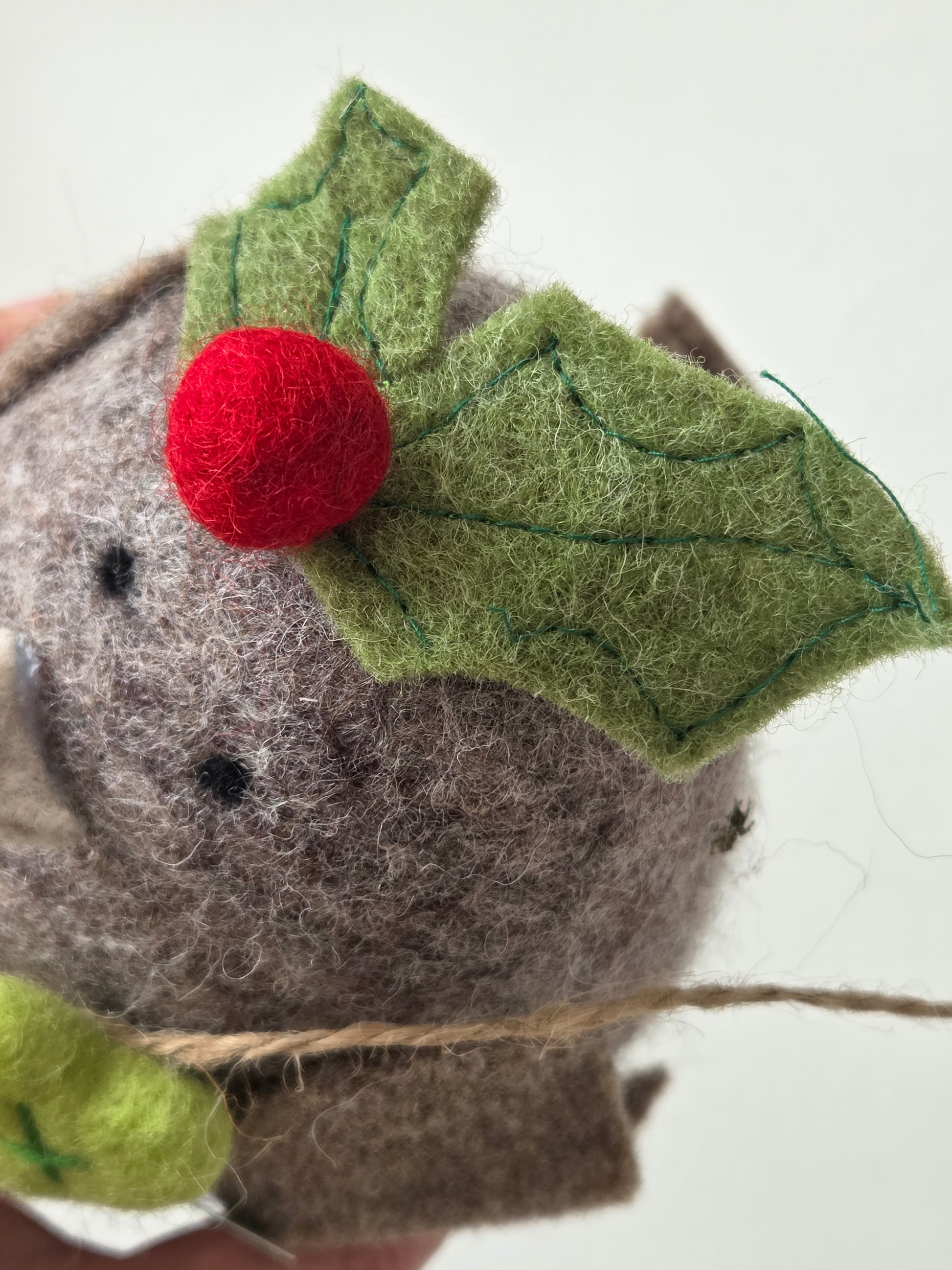 Felted animal ornament with holly leaf and berry on a white background