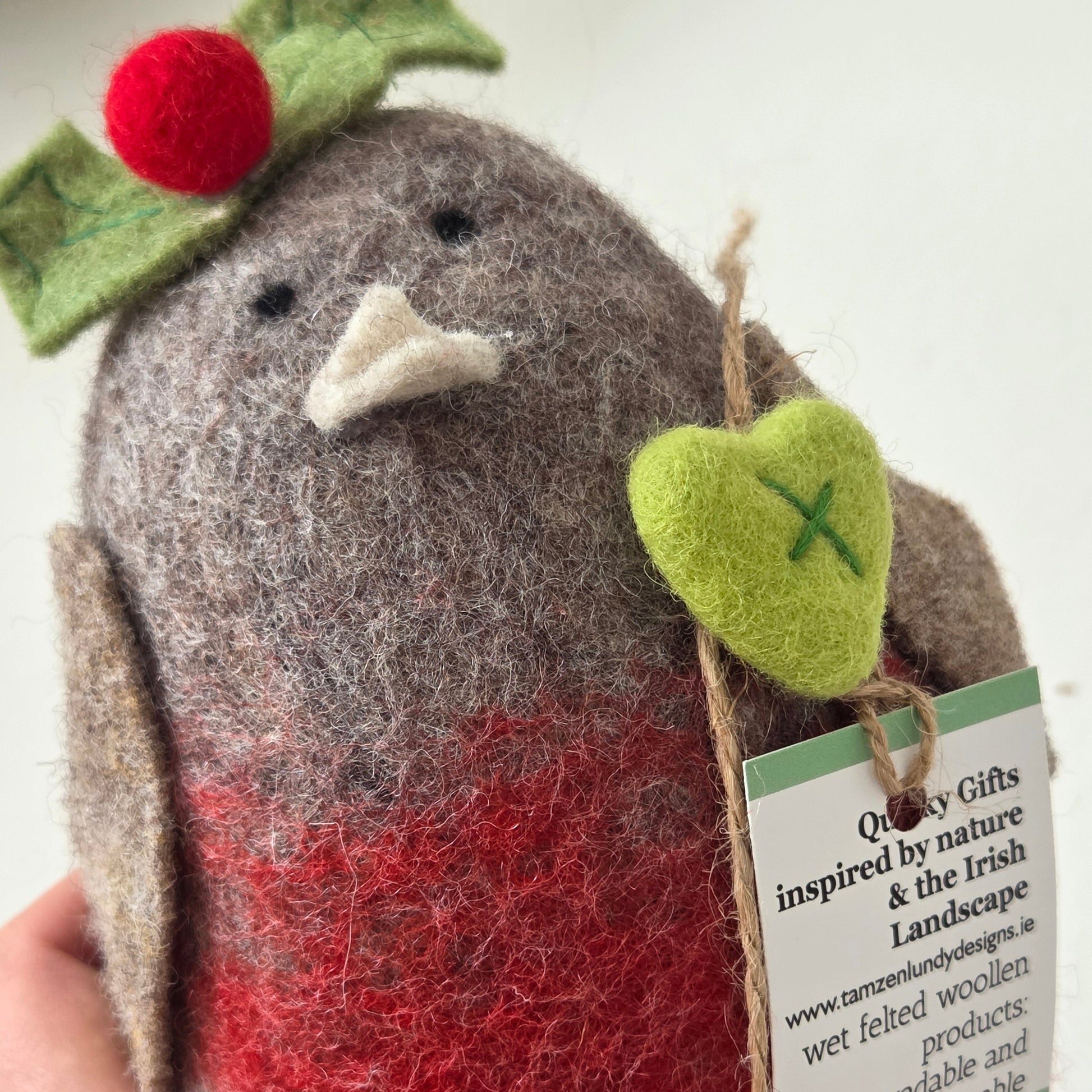 Felted animal toy with a green heart and red nose, held by a hand.