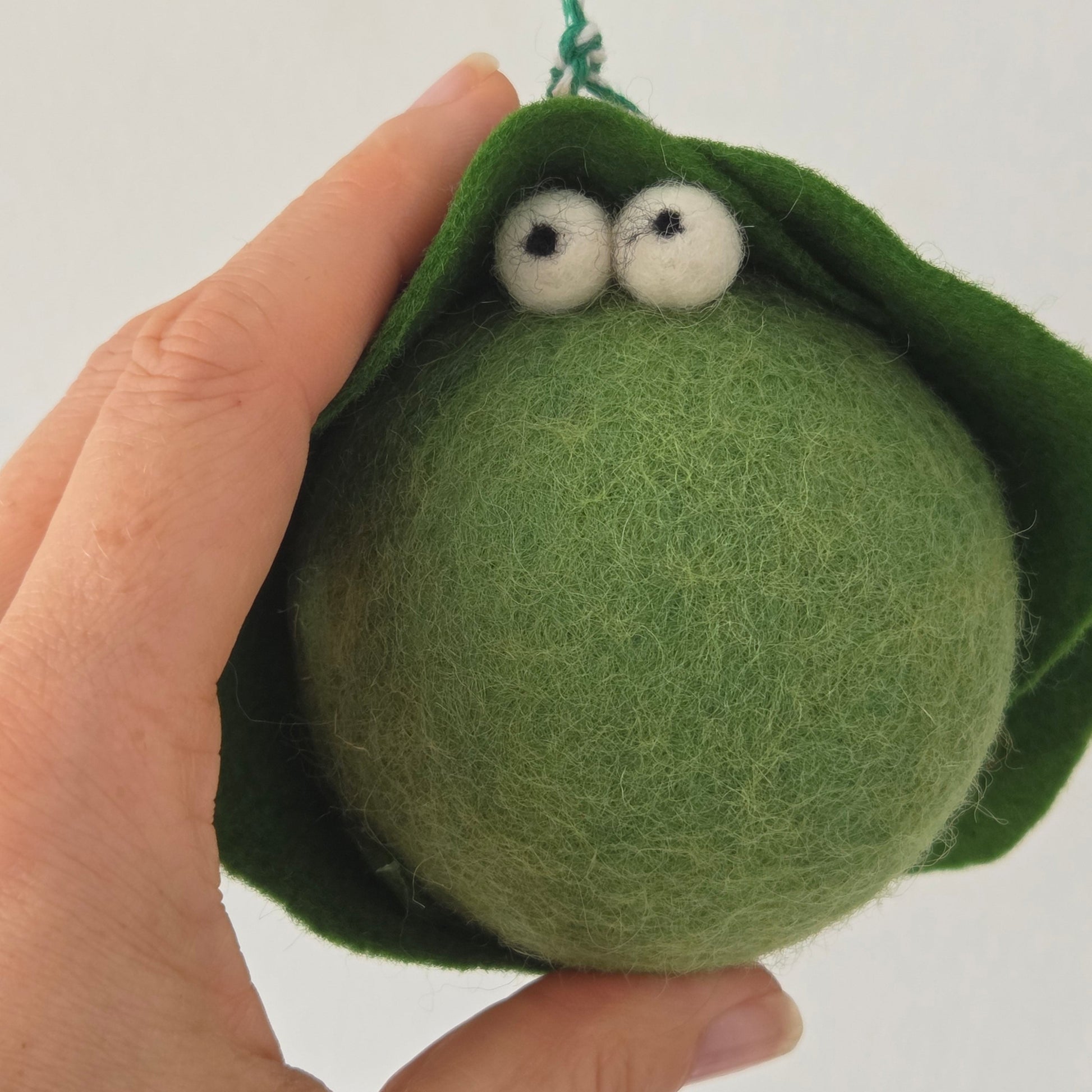 Green felted ball with googly eyes held in a hand against a white background