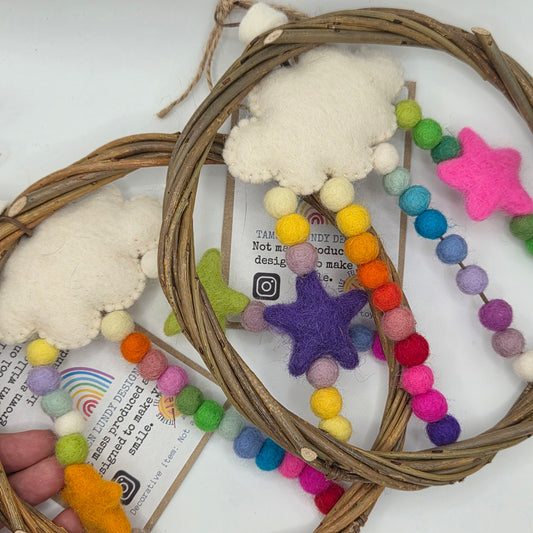 Decorative wreath with colorful pom-pom beads and felt cloud and star shapes on a white background.