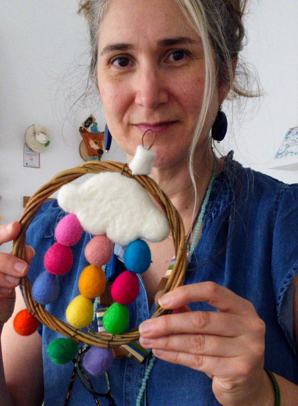 Woman holding a colorful woven craft with pom-poms and a cloud decoration.