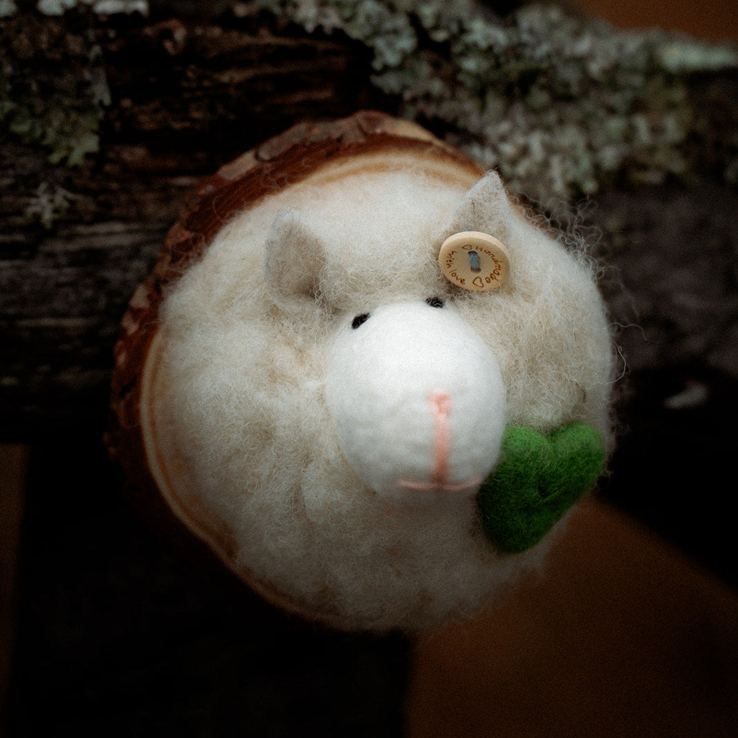 Small plush decorative wool sheep on a branch with a blurred background