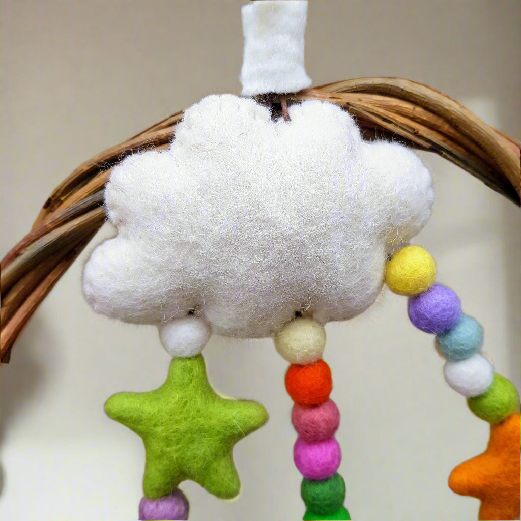 Felt cloud toy with colorful beads and stars held by a hand against a neutral background