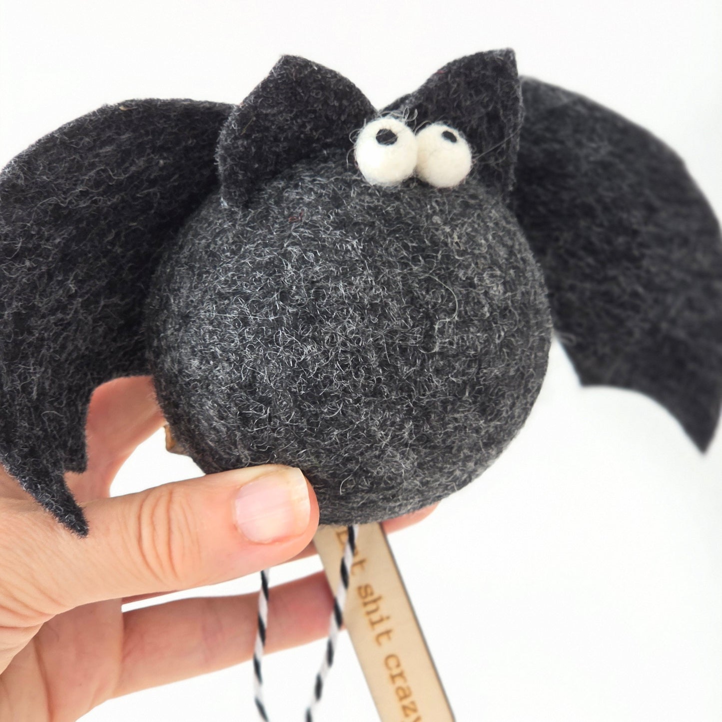 Hand holding a small black and gray plush toy with a stick, on a white background
