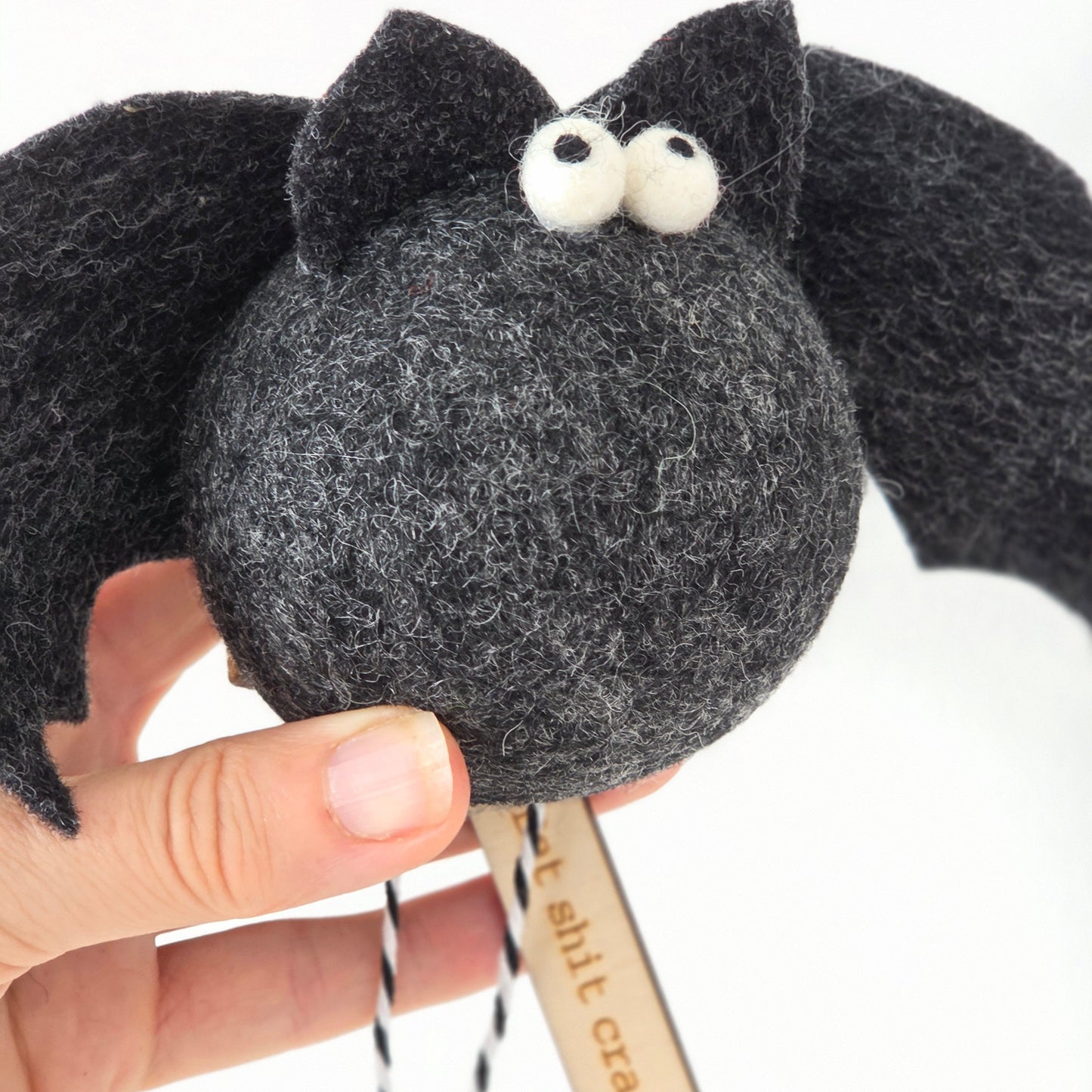 Black plush toy resembling a cat held by a hand with a white background