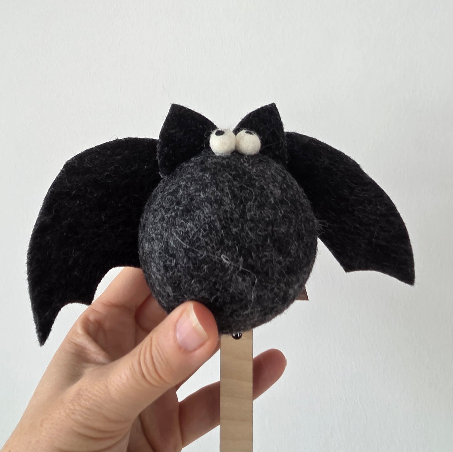Hand holding a small felt bat toy against a plain background