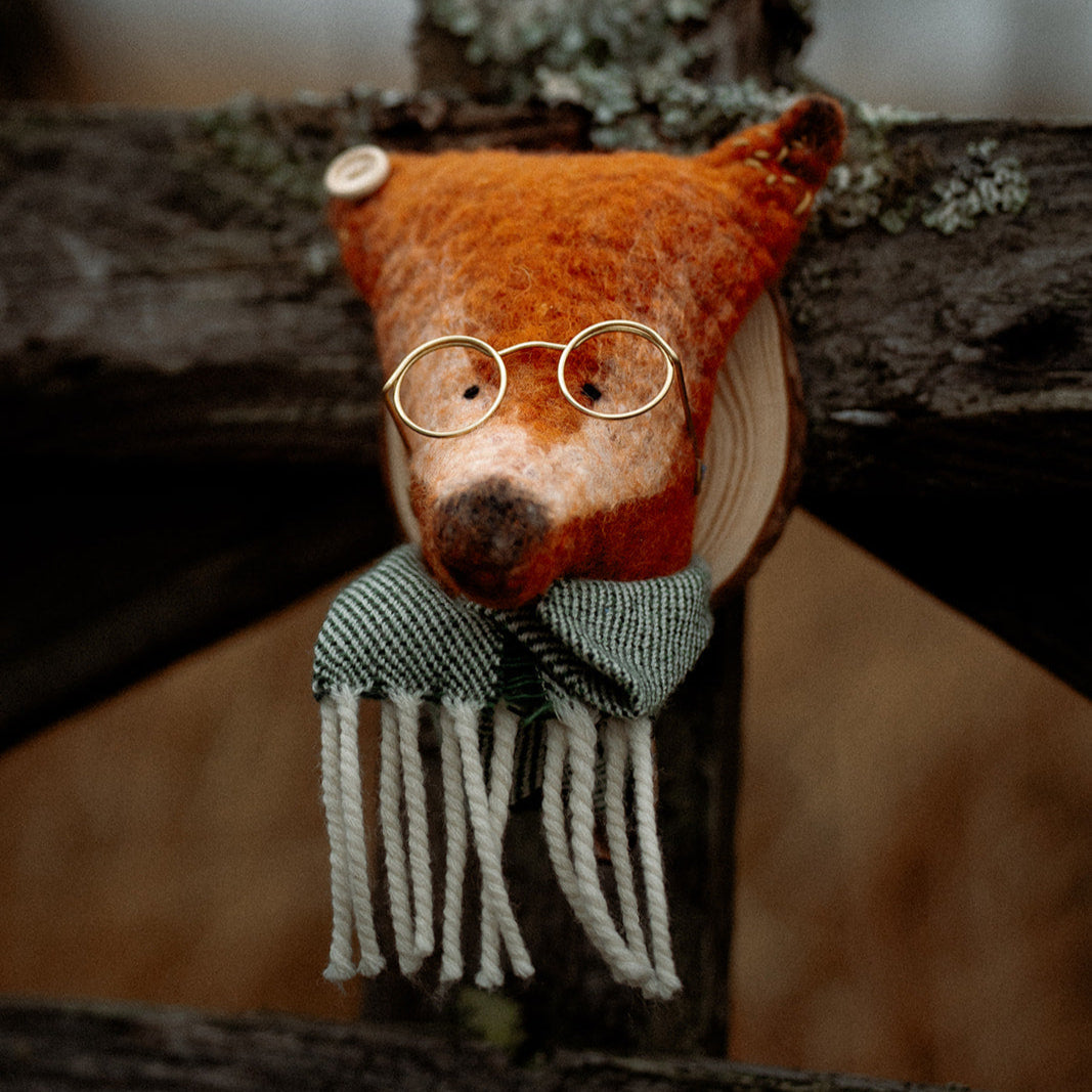 Stuffed animal fox wearing glasses and a scarf on a wooden surface