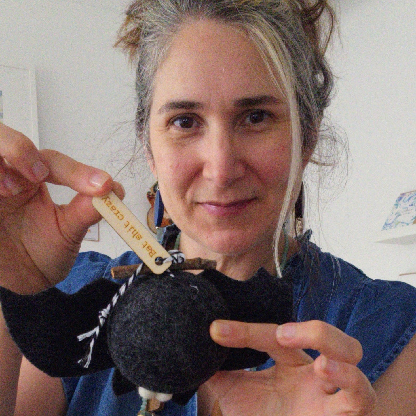 Person holding a small object with a label, wearing a blue shirt and green pants.