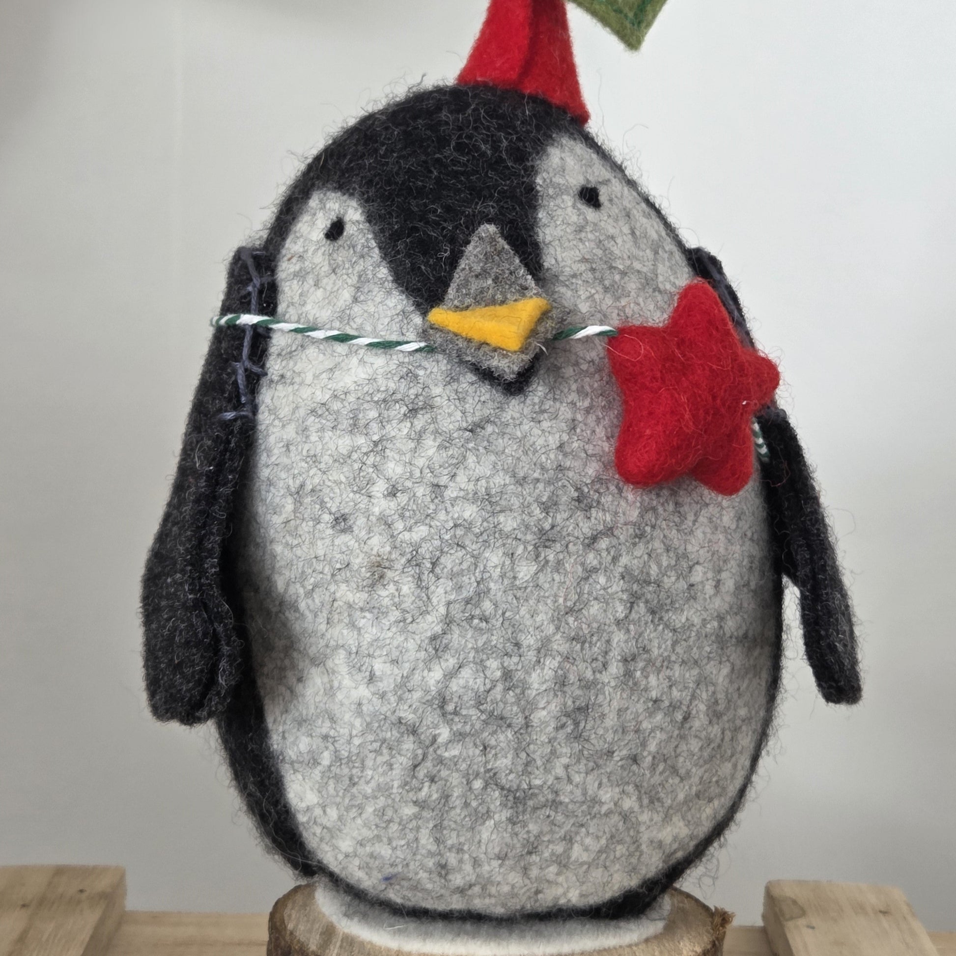 Felted penguin ornament with a Santa hat and red star on a wooden base.