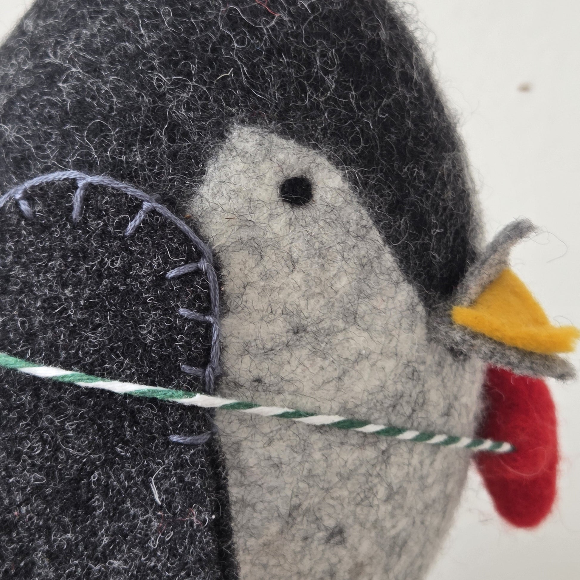 Felted penguin ornament with a red beak and black eyes on a white background