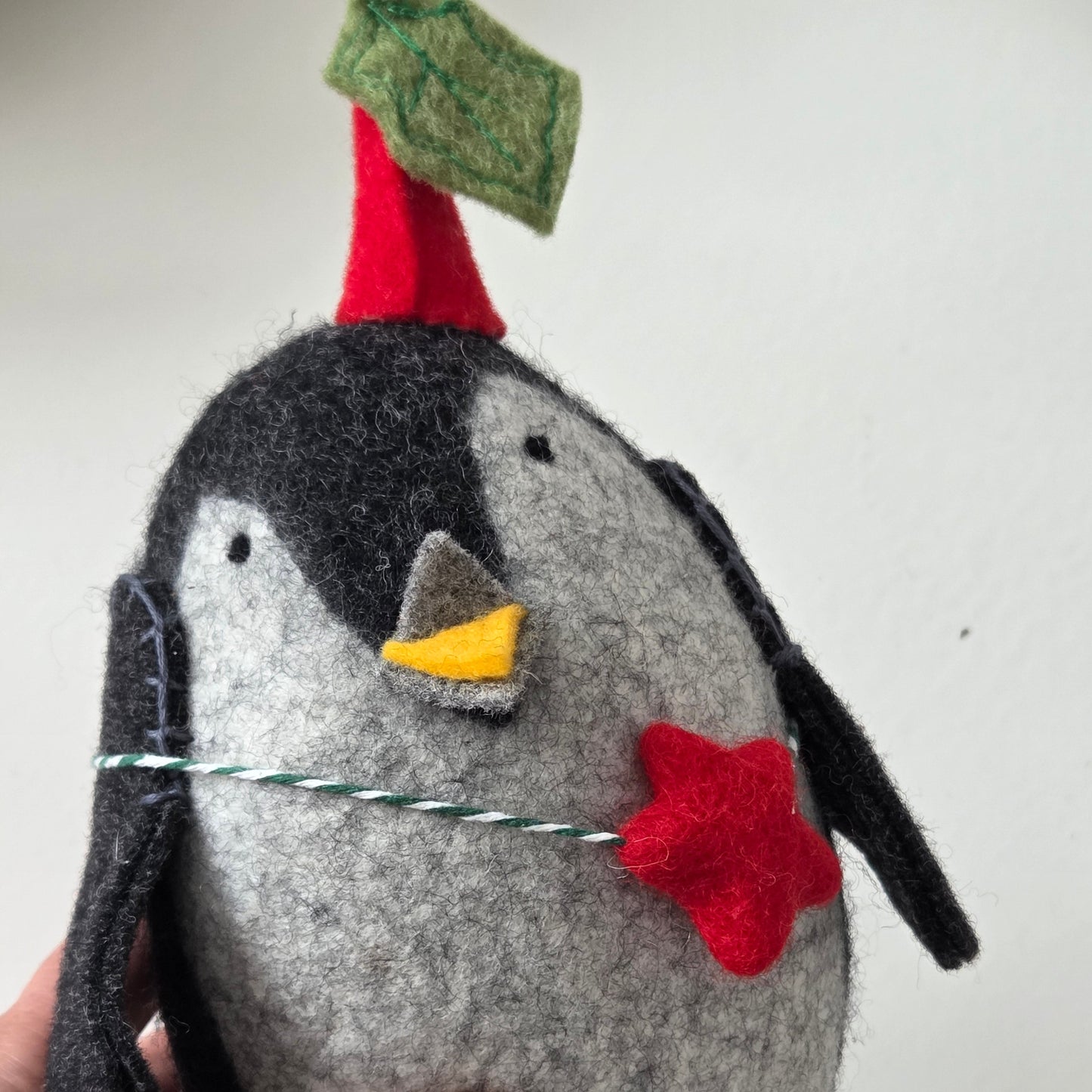 Handmade felt penguin with a red bow tie held by a hand against a white background