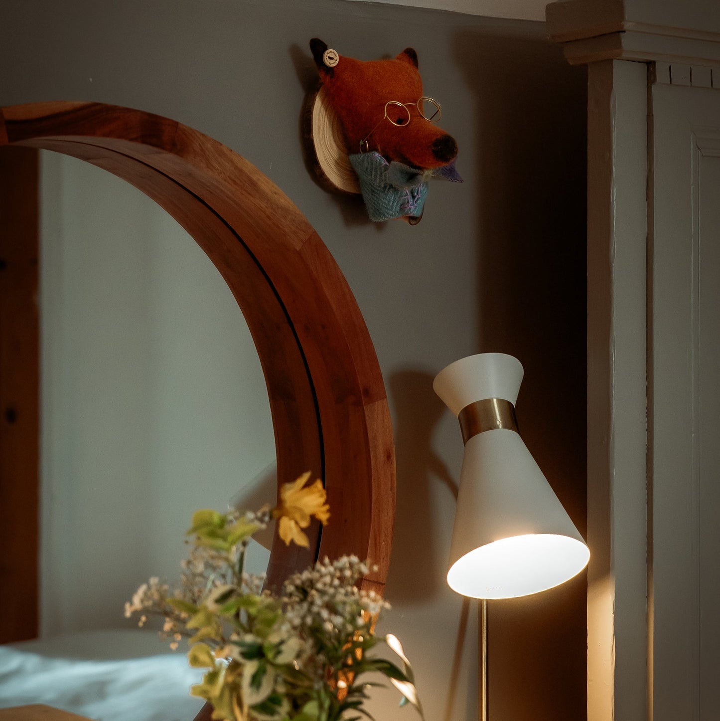 Room interior with a mirror, lamp, and decorative items on a shelf.