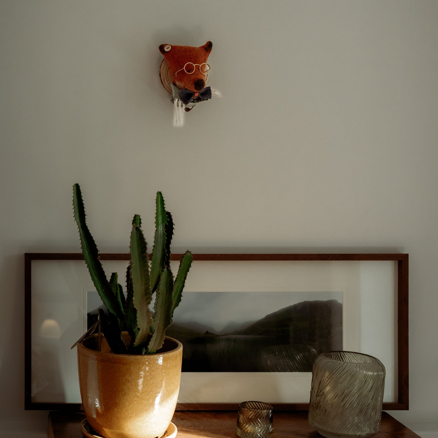 Small fox sculpture on a wall above a potted plant and framed picture.