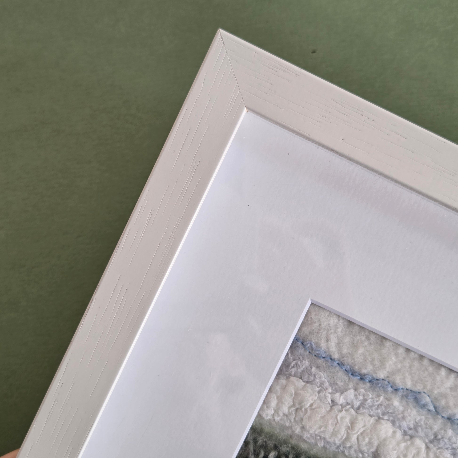 Close-up of a white picture frame corner on a green surface