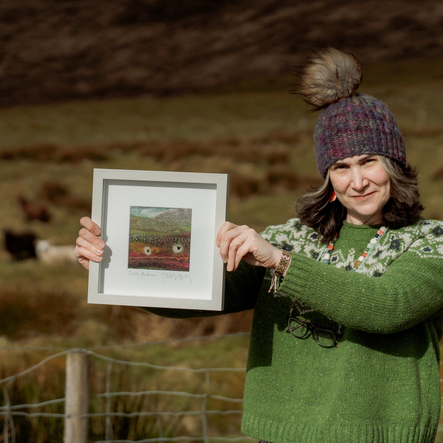 Woman holding a framed picture in a field with sheep in the background