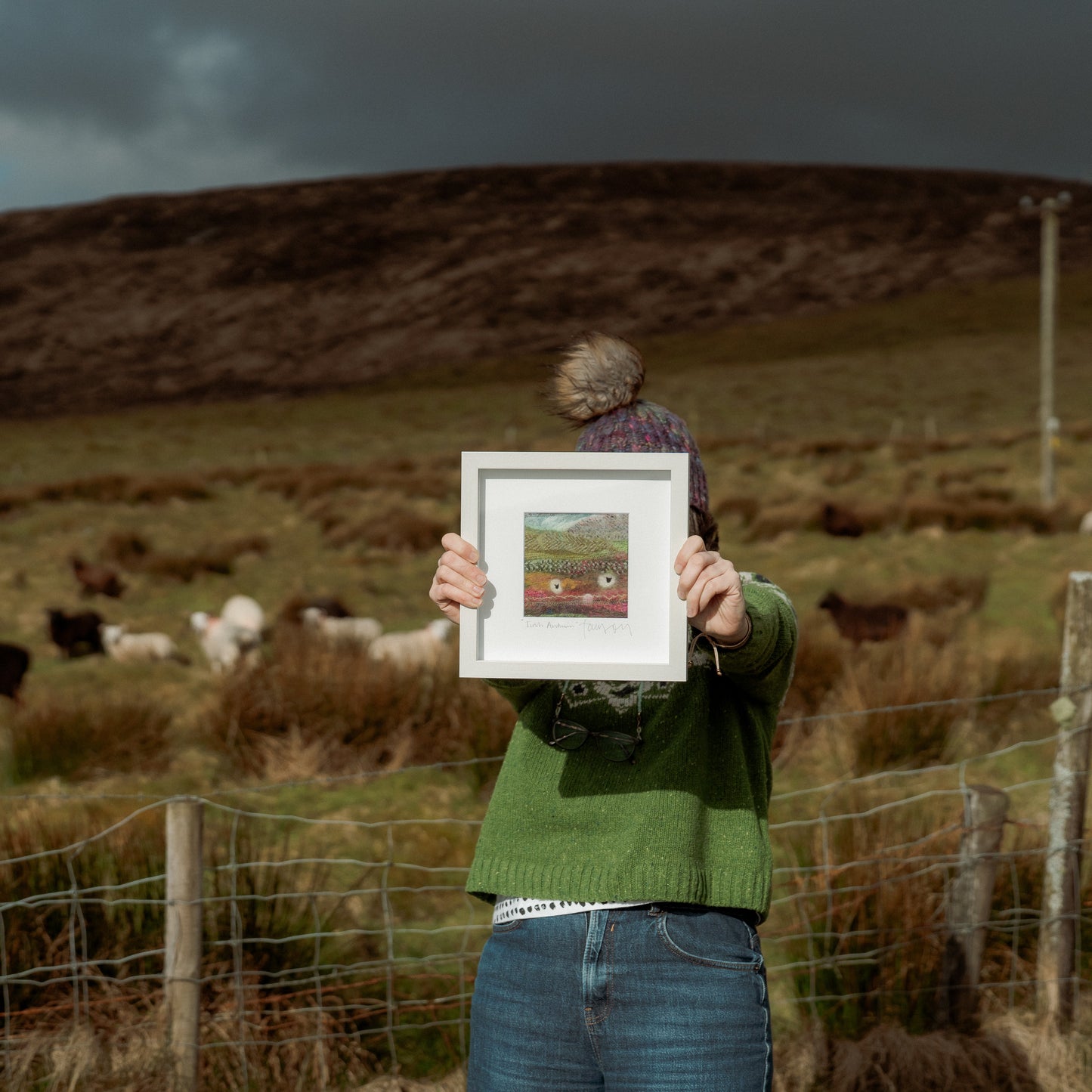 Person holding a framed picture of a landscape with sheep in a field