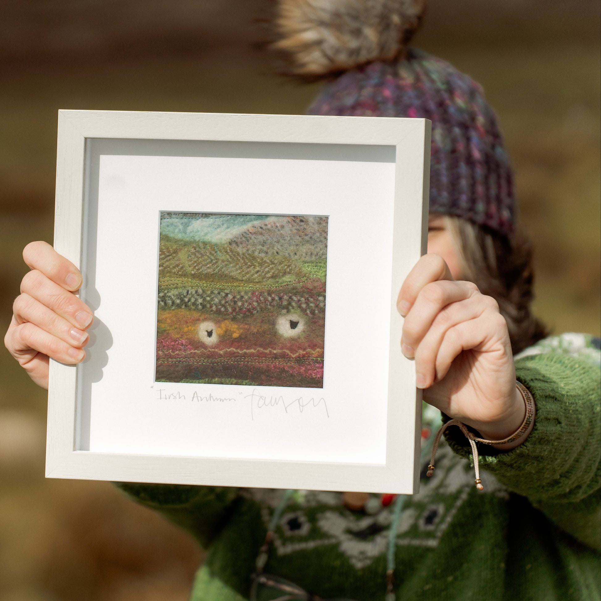 Person holding a framed woven artwork outdoors