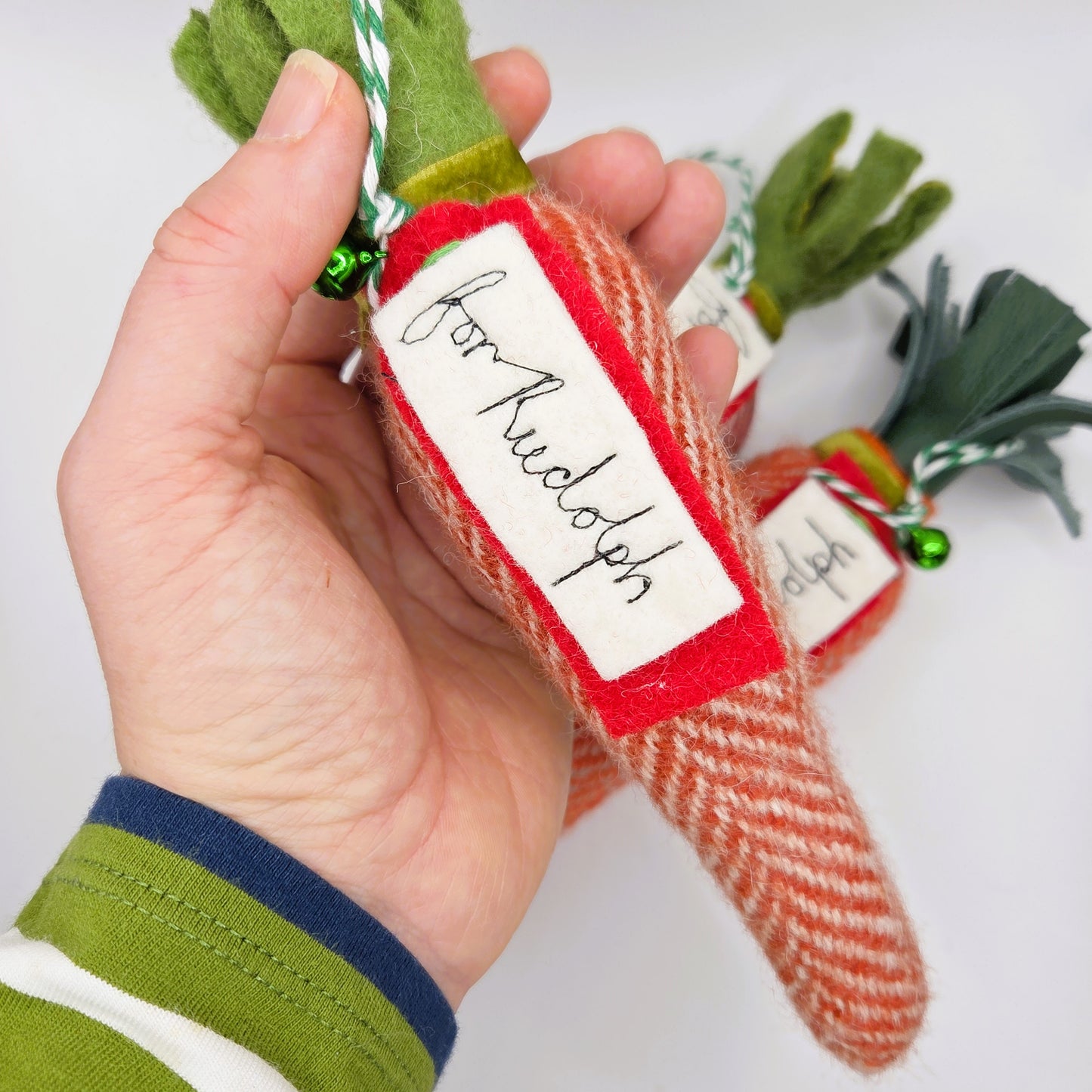 Hand holding a small Christmas ornament shaped like a carrot with a tag on a white background