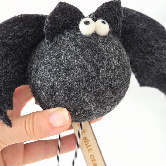 Black plush toy resembling a cat held by a hand with a white background